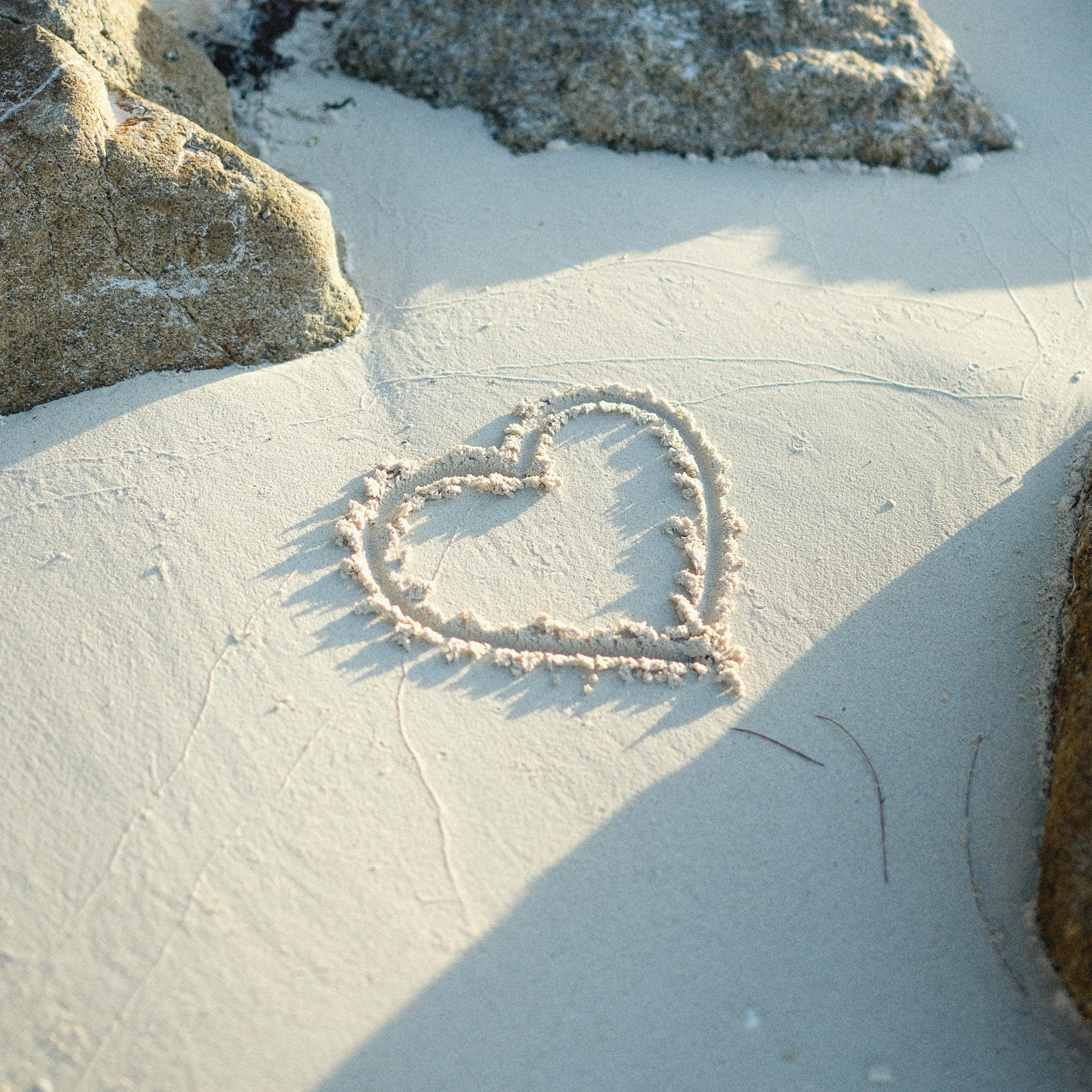 Heart shape drawn in sand with rocks around